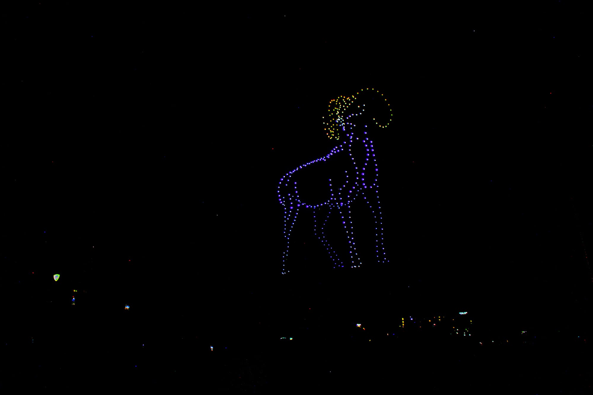 A drone display shows a full-body blue ram with yellow horns in the night sky. 
