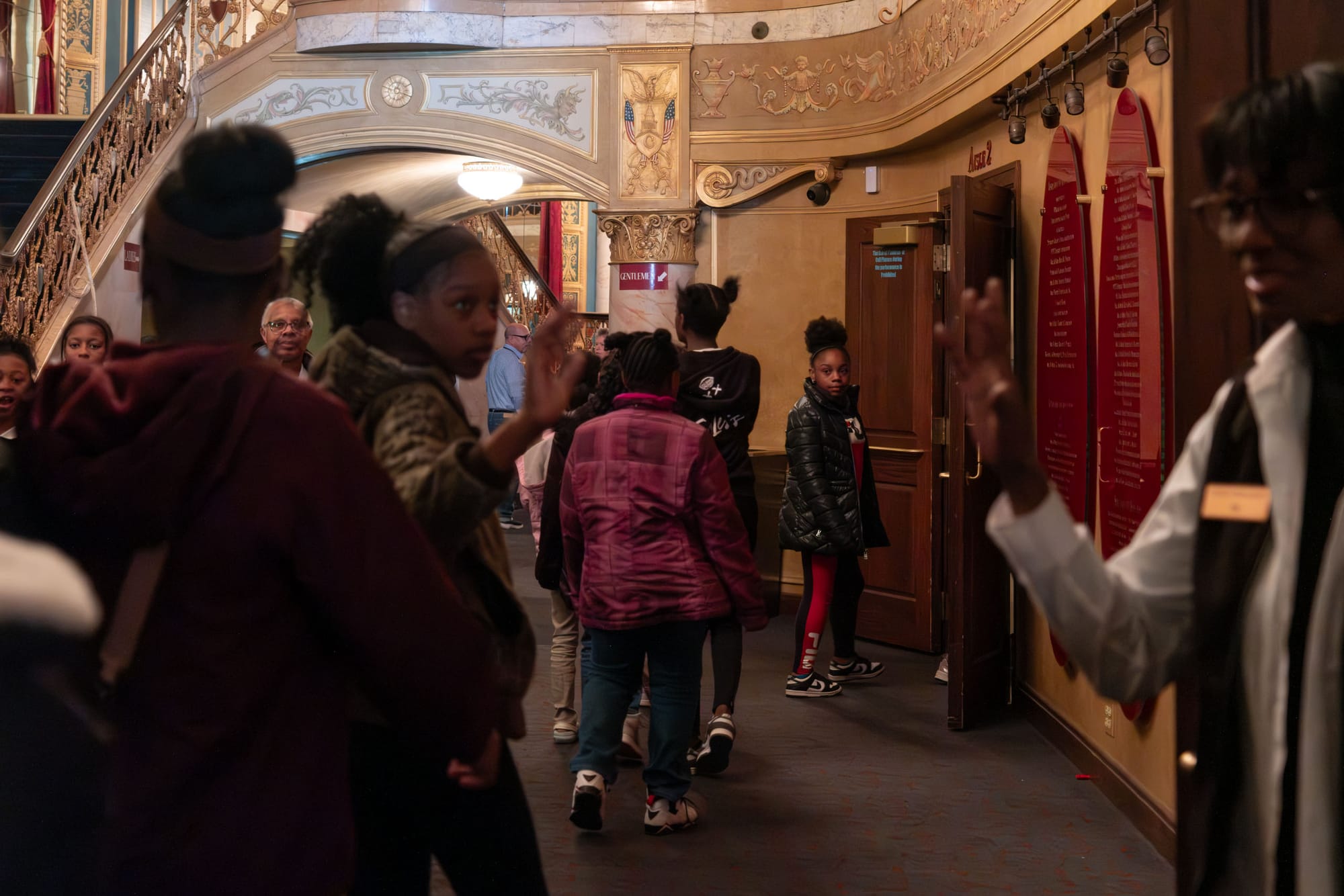 A group of people walk in a line through the lobby area of a building.