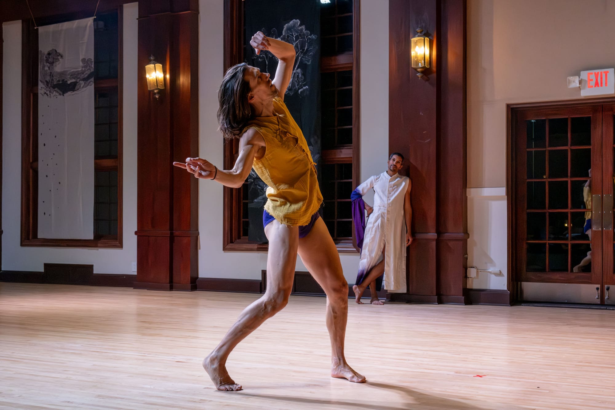 Two people stand across from each other, one leans on the wall the other is in front and leans his hands back. 