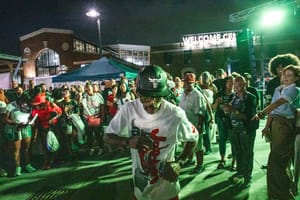 A man in a graphic t-shirt and cap dances under green lights at an outdoor night event.